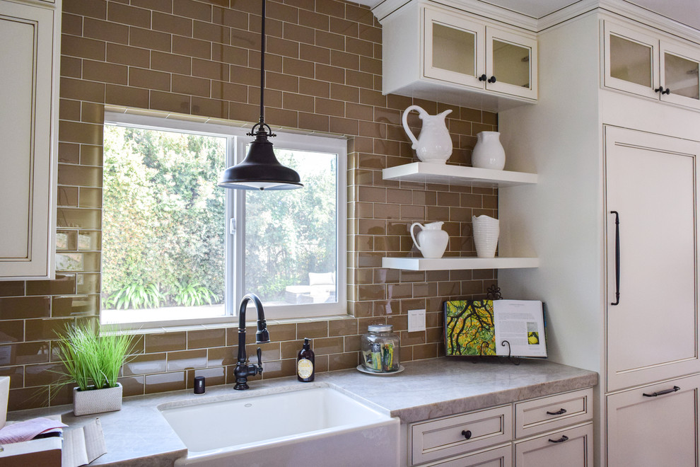 This is an example of a mid-sized transitional kitchen in Orange County with a farmhouse sink, recessed-panel cabinets, white cabinets, marble benchtops, brown splashback, subway tile splashback and panelled appliances.