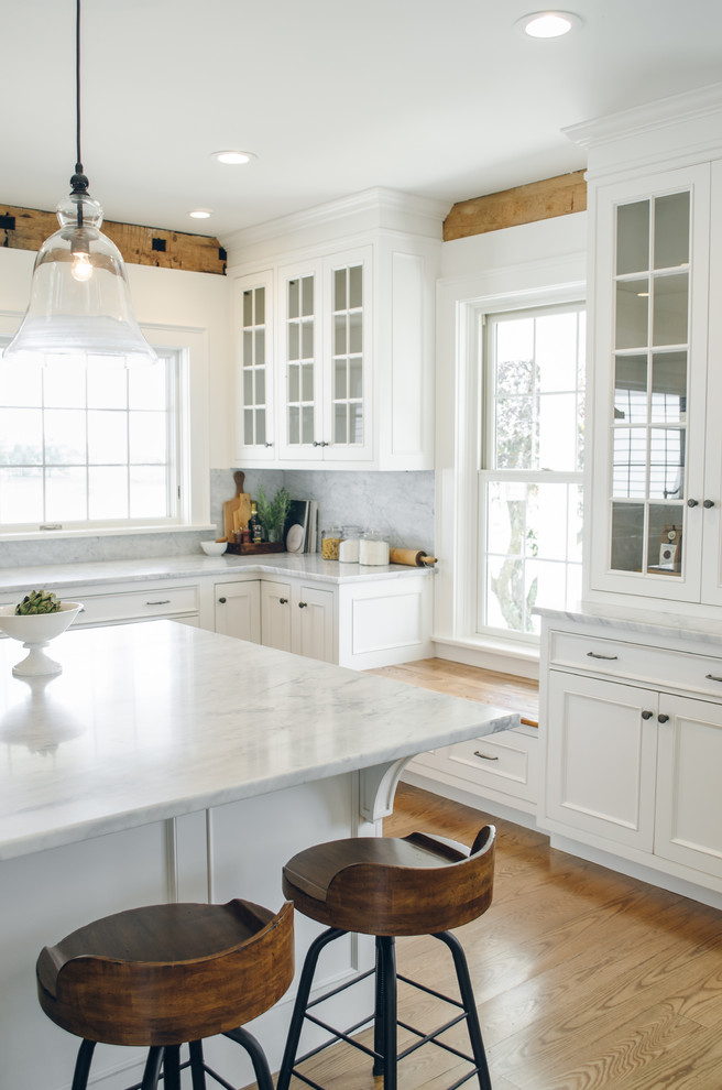 Large country u-shaped eat-in kitchen in New York with a farmhouse sink, beaded inset cabinets, white cabinets, white splashback, stainless steel appliances, medium hardwood floors, with island and marble benchtops.