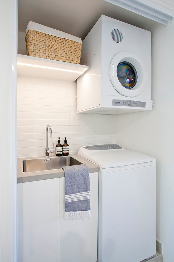 Small contemporary single-wall dedicated laundry room in Sunshine Coast with a drop-in sink, flat-panel cabinets, white cabinets, quartz benchtops, white walls, porcelain floors, a stacked washer and dryer and grey floor.