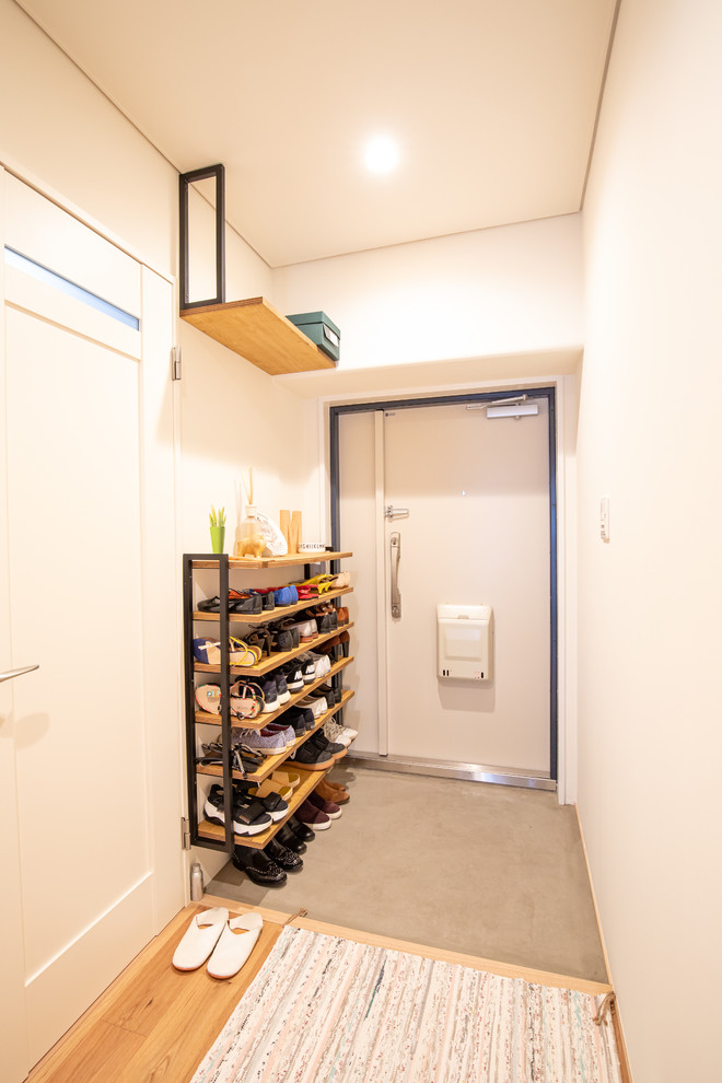 This is an example of a small asian entry hall in Osaka with white walls, concrete floors, a single front door, a white front door and grey floor.