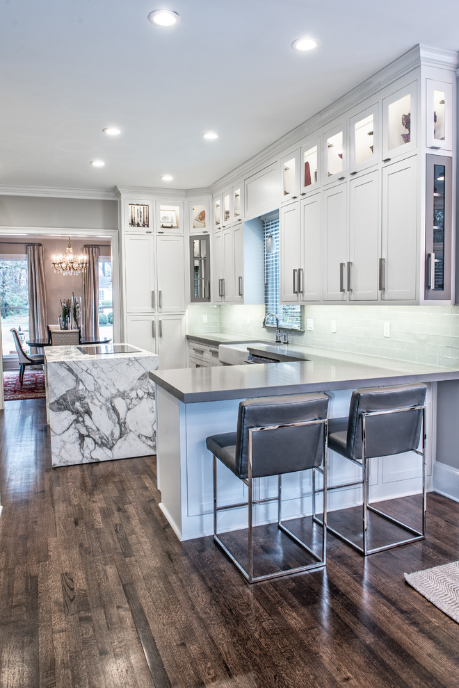 Enclosed kitchen - large transitional l-shaped dark wood floor enclosed kitchen idea with a farmhouse sink, stainless steel appliances, shaker cabinets, white cabinets, solid surface countertops, white backsplash, subway tile backsplash and an island