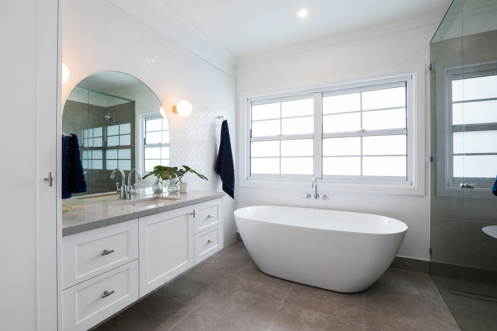 This is an example of a beach style bathroom in Gold Coast - Tweed with shaker cabinets, white cabinets, a freestanding tub, white walls, an undermount sink, grey floor and grey benchtops.
