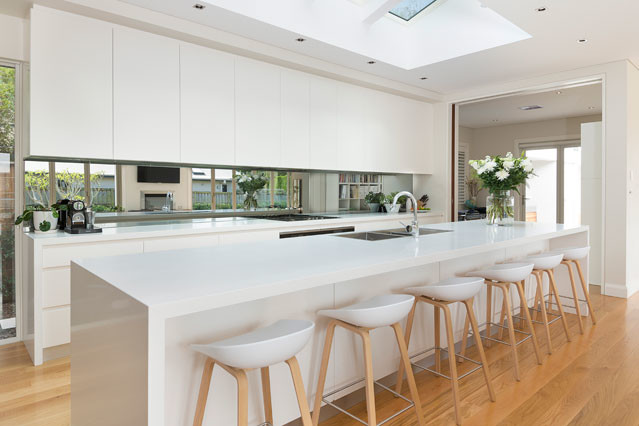 Design ideas for a contemporary single-wall kitchen in Sydney with flat-panel cabinets, white cabinets, granite benchtops, mirror splashback, light hardwood floors and with island.