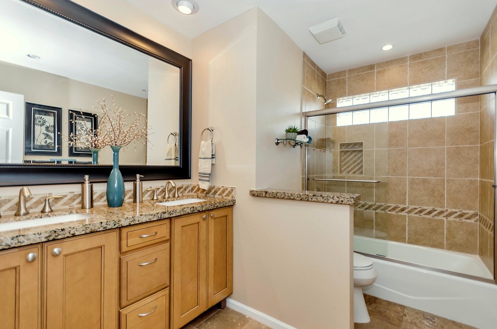 Mid-sized mediterranean kids bathroom in Phoenix with an undermount sink, recessed-panel cabinets, medium wood cabinets, granite benchtops, a drop-in tub, an alcove shower, a two-piece toilet, beige tile, subway tile, beige walls and travertine floors.