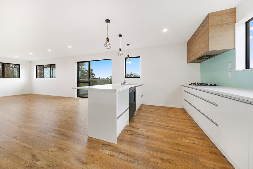 Design ideas for a mid-sized contemporary eat-in kitchen in Auckland with an undermount sink, light wood cabinets, quartz benchtops, white splashback, glass sheet splashback, stainless steel appliances, medium hardwood floors, with island, brown floor and white benchtop.