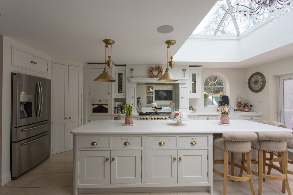 Large traditional l-shaped eat-in kitchen in Hertfordshire with a single-bowl sink, shaker cabinets, yellow cabinets, soapstone benchtops, metallic splashback, mirror splashback, stainless steel appliances, porcelain floors, with island, beige floor and white benchtop.