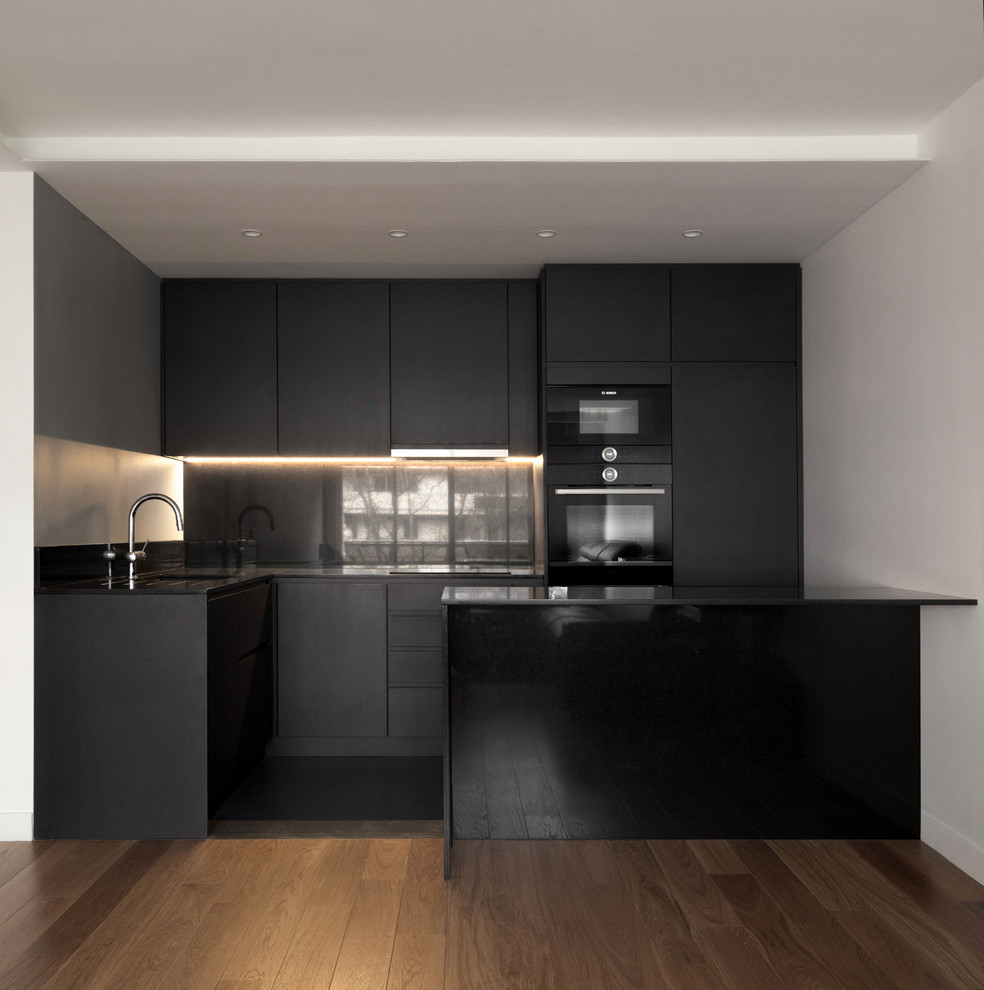 Design ideas for a mid-sized modern l-shaped open plan kitchen in Paris with an undermount sink, beaded inset cabinets, grey cabinets, granite benchtops, grey splashback, granite splashback, black appliances, concrete floors, with island, grey floor and grey benchtop.