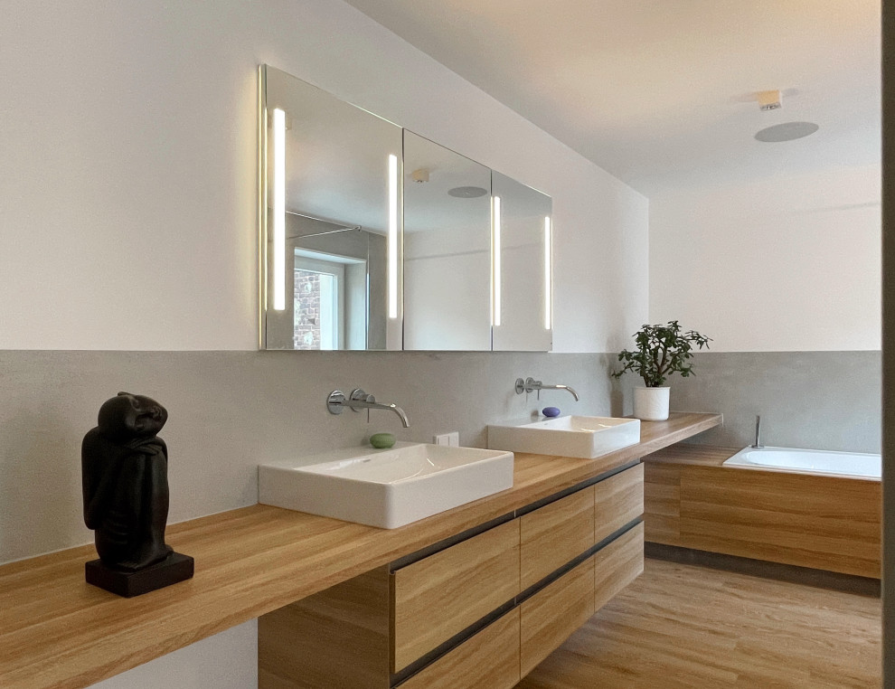 Photo of a mid-sized contemporary bathroom in Cologne with flat-panel cabinets, light wood cabinets, a drop-in tub, an open shower, a wall-mount toilet, gray tile, white walls, vinyl floors, a vessel sink, an open shower, a niche, a double vanity and a built-in vanity.