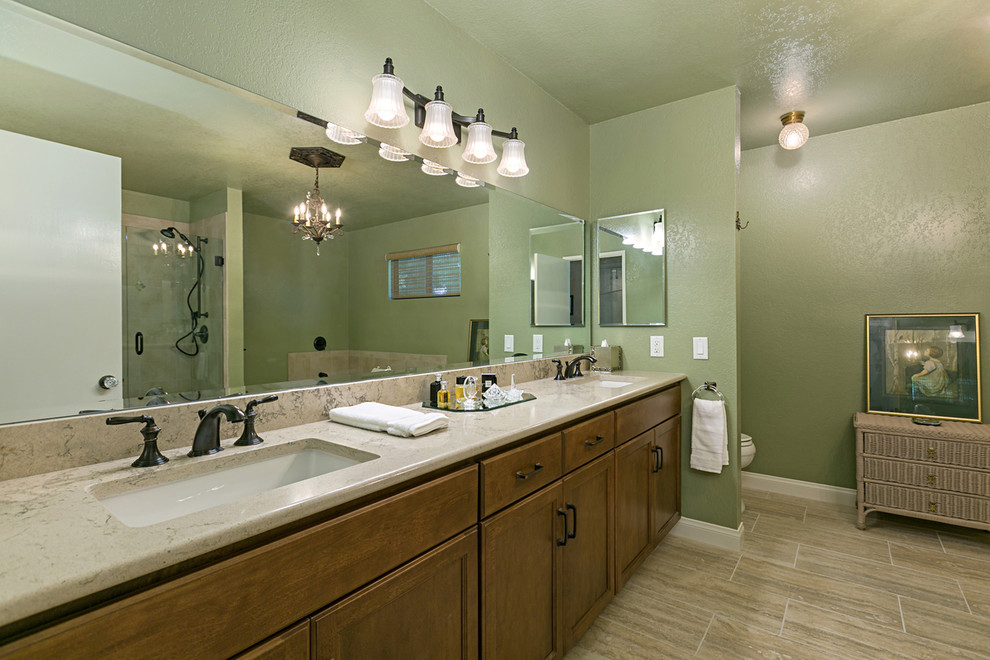 This is an example of a large traditional master bathroom in San Diego with recessed-panel cabinets, dark wood cabinets, a corner tub, a corner shower, a two-piece toilet, black tile, travertine, green walls, porcelain floors, an undermount sink, granite benchtops, brown floor, a hinged shower door, beige benchtops, a double vanity and a built-in vanity.