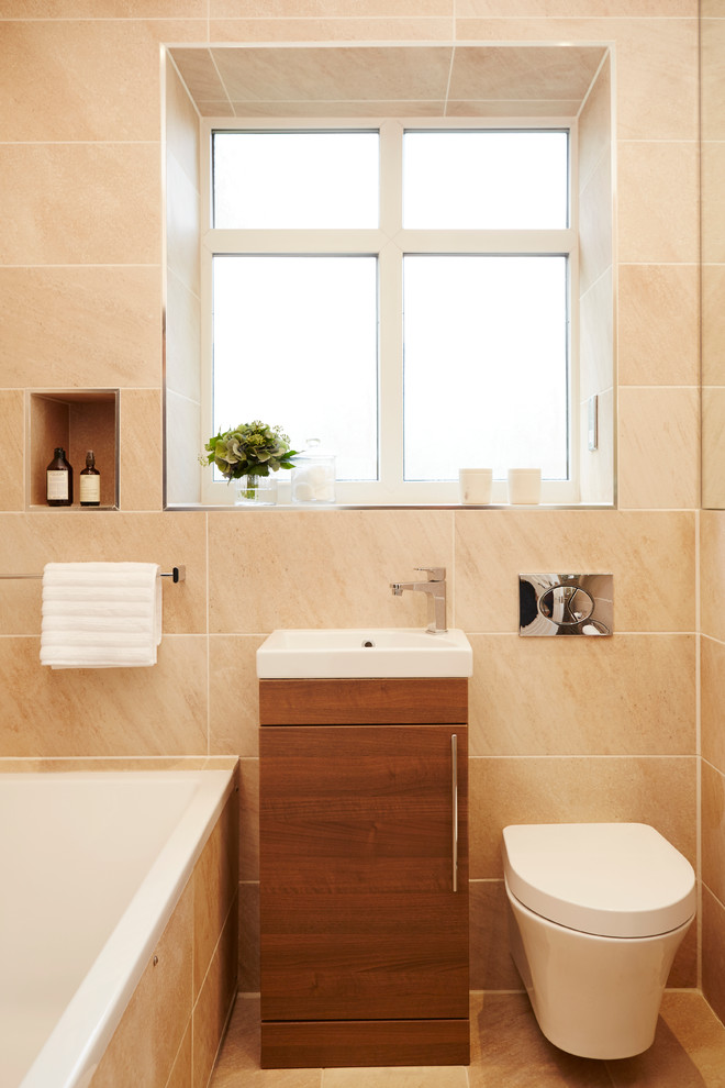 Inspiration for a small contemporary family bathroom in London with freestanding cabinets, medium wood cabinets, a built-in bath, a shower/bath combination, a wall mounted toilet, beige tiles, ceramic tiles, beige walls, ceramic flooring and an integrated sink.