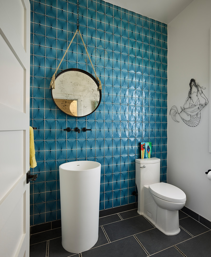 Small beach style powder room in San Francisco with a one-piece toilet, blue tile, blue walls, a pedestal sink, grey floor, white cabinets and glass tile.