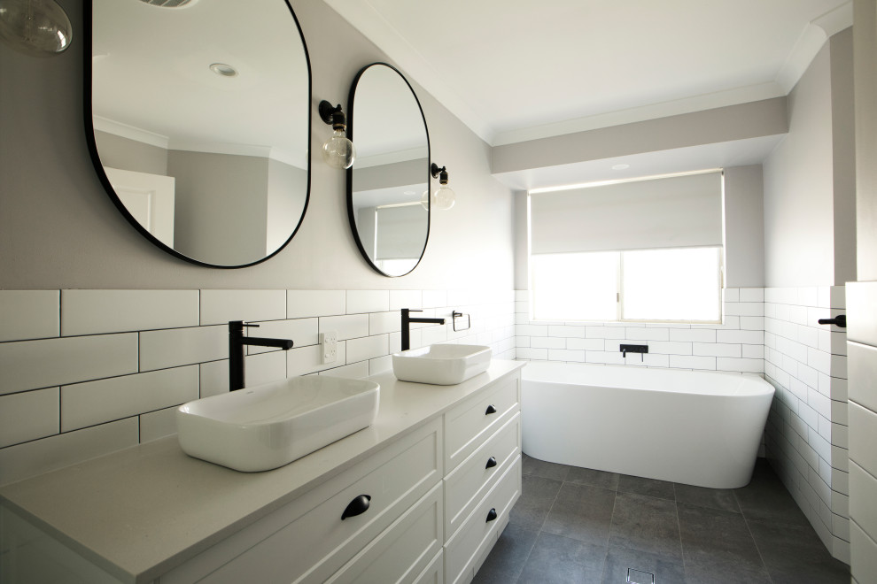 This is an example of a mid-sized industrial master bathroom in Perth with recessed-panel cabinets, white cabinets, a corner shower, white tile, subway tile, white walls, ceramic floors, a vessel sink, black floor, an open shower and white benchtops.
