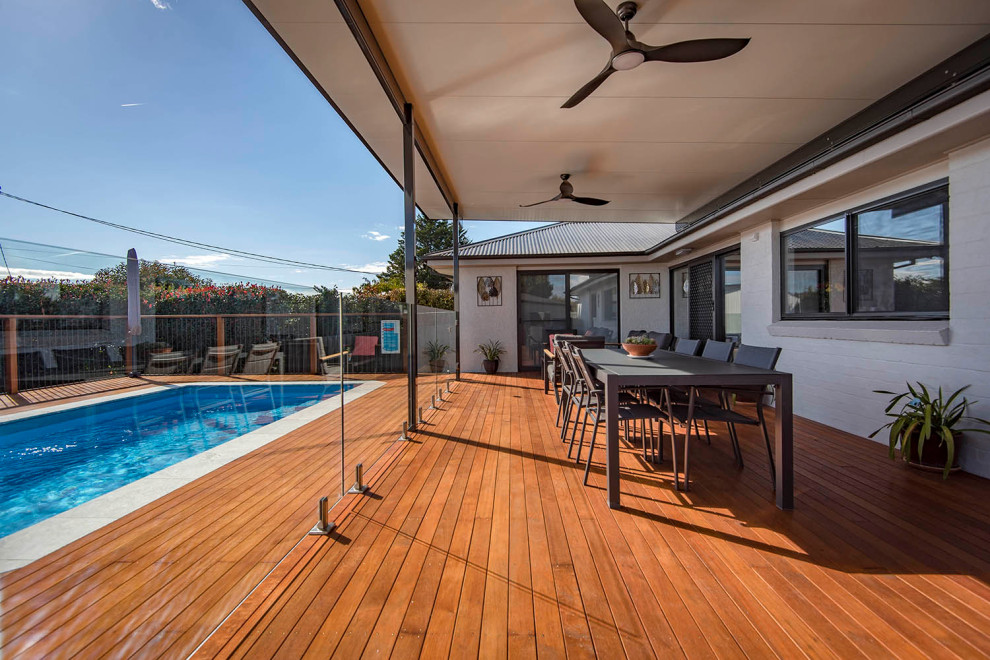 This is an example of a large contemporary backyard deck in Canberra - Queanbeyan with a pergola and glass railing.