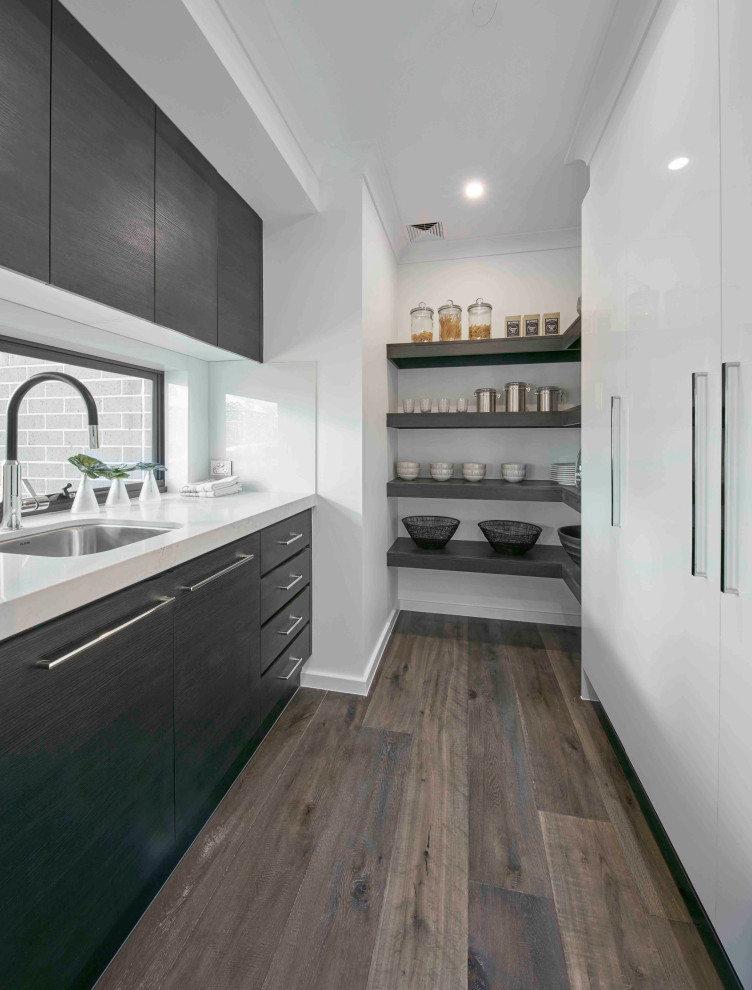 Photo of a contemporary single-wall kitchen pantry in Sydney with with island, an undermount sink, flat-panel cabinets, white cabinets, white splashback, stainless steel appliances, medium hardwood floors, brown floor and white benchtop.
