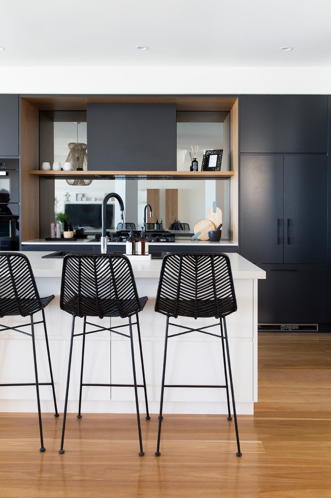 Inspiration for a large contemporary galley eat-in kitchen in Gold Coast - Tweed with a drop-in sink, flat-panel cabinets, light wood cabinets, quartz benchtops, mirror splashback, black appliances, light hardwood floors, with island and brown floor.