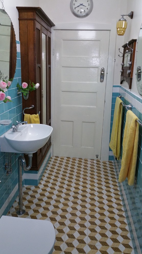 Small midcentury 3/4 bathroom in Sydney with a wall-mount sink, furniture-like cabinets, medium wood cabinets, a drop-in tub, a shower/bathtub combo, a two-piece toilet, blue tile, ceramic tile, blue walls and travertine floors.