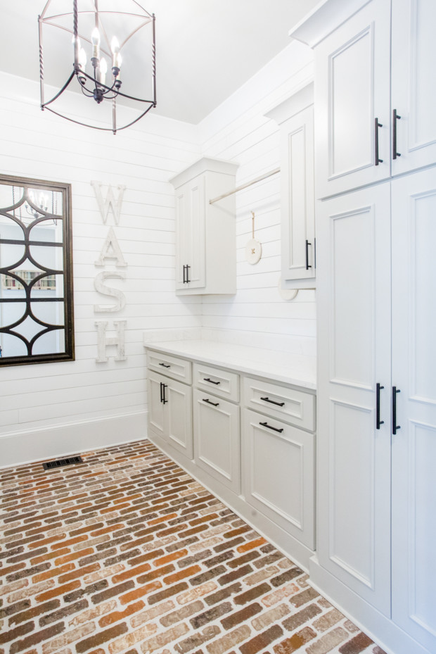 Design ideas for a large transitional galley utility room in Atlanta with a farmhouse sink, raised-panel cabinets, grey cabinets, quartz benchtops, white walls, brick floors, a side-by-side washer and dryer, red floor and white benchtop.