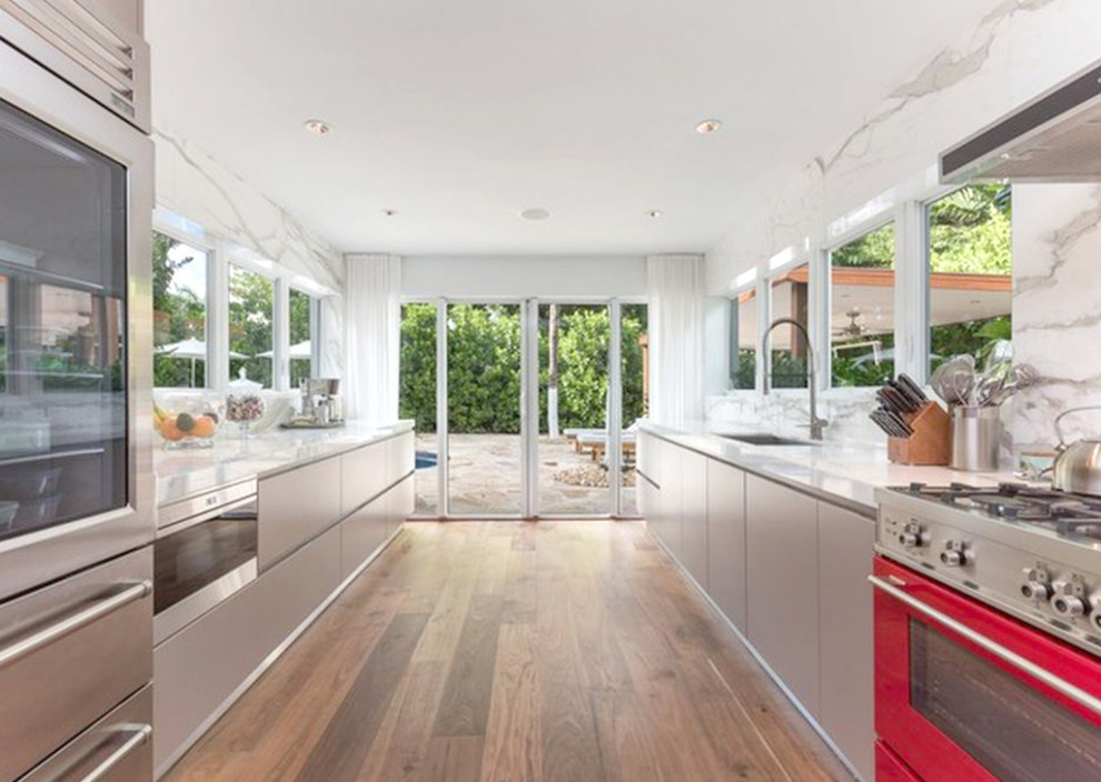 Photo of a large modern galley eat-in kitchen in Miami with a single-bowl sink, flat-panel cabinets, grey cabinets, marble benchtops, grey splashback, marble splashback, coloured appliances, medium hardwood floors, no island, brown floor and grey benchtop.