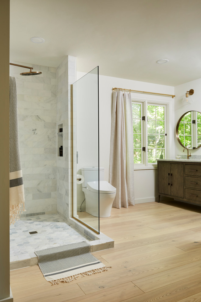 Photo of a mid-sized modern master bathroom in Minneapolis with flat-panel cabinets, brown cabinets, an open shower, a bidet, white tile, marble, an integrated sink, marble benchtops, an open shower, white benchtops, a double vanity, a freestanding vanity, white walls, light hardwood floors and beige floor.