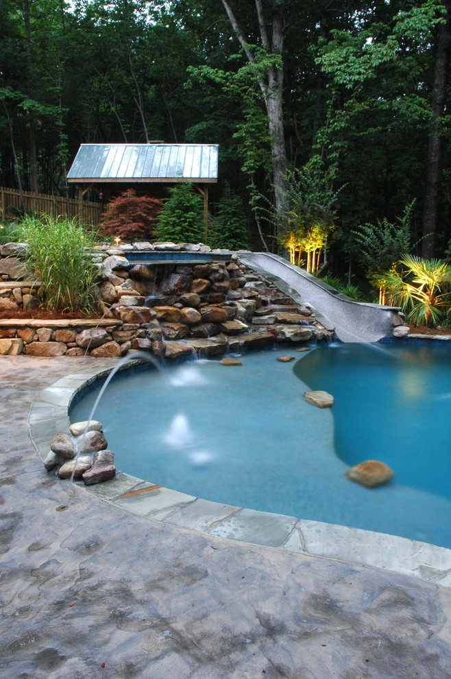 This is an example of a large country backyard kidney-shaped infinity pool in Atlanta with a water slide.