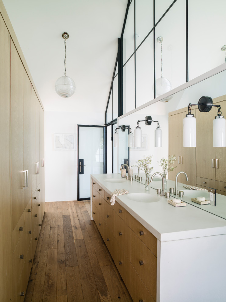 This is an example of a beach style bathroom in DC Metro with flat-panel cabinets, medium wood cabinets, white walls, medium hardwood floors, an integrated sink, brown floor, white benchtops, a double vanity, a built-in vanity and vaulted.