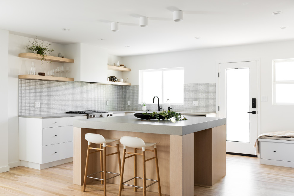 This is an example of a small scandinavian l-shaped eat-in kitchen in Salt Lake City with a farmhouse sink, flat-panel cabinets, light wood cabinets, quartz benchtops, grey splashback, mosaic tile splashback, stainless steel appliances, light hardwood floors, with island, beige floor and grey benchtop.