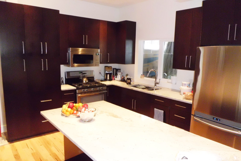 Example of a large l-shaped light wood floor eat-in kitchen design with a drop-in sink, dark wood cabinets, stainless steel appliances and an island