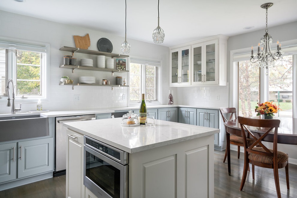 Photo of a large country u-shaped eat-in kitchen in Columbus with a farmhouse sink, raised-panel cabinets, white cabinets, quartzite benchtops, white splashback, subway tile splashback, stainless steel appliances, medium hardwood floors, with island and grey floor.