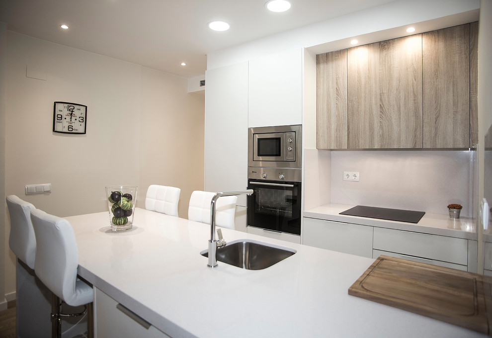 Photo of a mid-sized contemporary galley open plan kitchen in Barcelona with a single-bowl sink, medium wood cabinets, white splashback, stainless steel appliances and no island.
