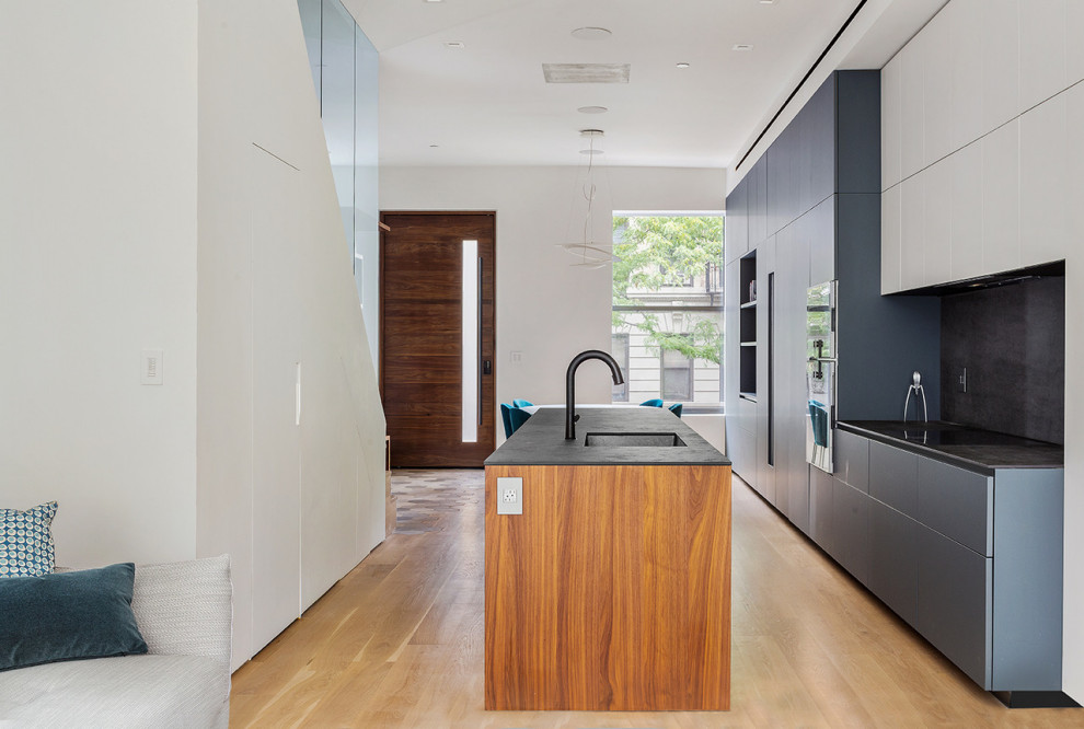 This is an example of a large contemporary single-wall open plan kitchen in New York with an undermount sink, flat-panel cabinets, grey cabinets, solid surface benchtops, grey splashback, porcelain splashback, panelled appliances, light hardwood floors, with island, beige floor and grey benchtop.
