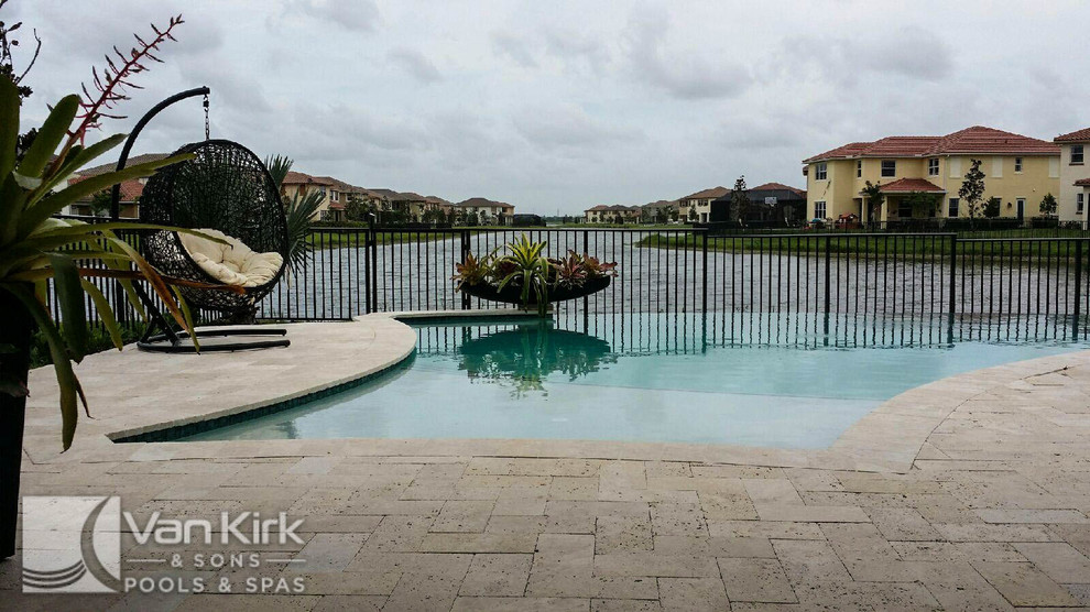 This is an example of a mid-sized contemporary backyard custom-shaped infinity pool in Miami with a water feature and natural stone pavers.
