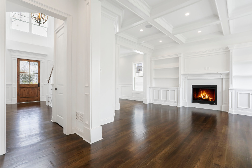 Inspiration for a mid-sized transitional open concept living room in New York with white walls, medium hardwood floors, a standard fireplace, a wood fireplace surround, a wall-mounted tv, brown floor, coffered and decorative wall panelling.