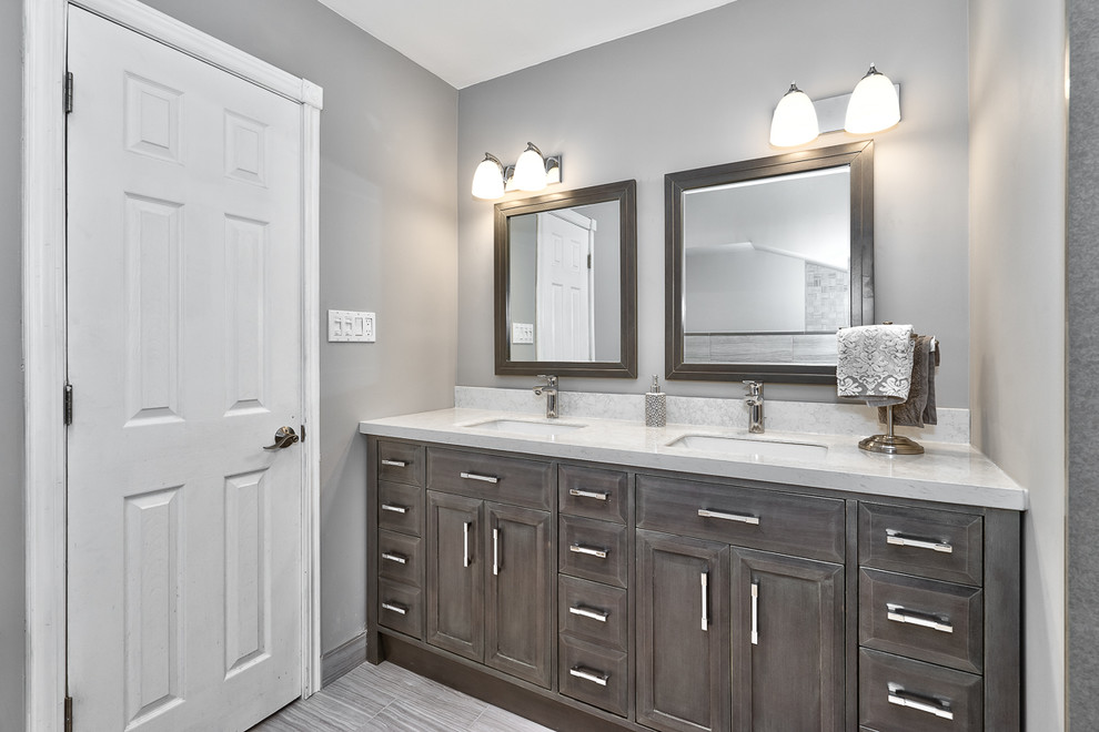 This is an example of a mid-sized transitional master bathroom in Toronto with shaker cabinets, distressed cabinets, a corner tub, a curbless shower, a two-piece toilet, gray tile, porcelain tile, grey walls, porcelain floors, an undermount sink and solid surface benchtops.