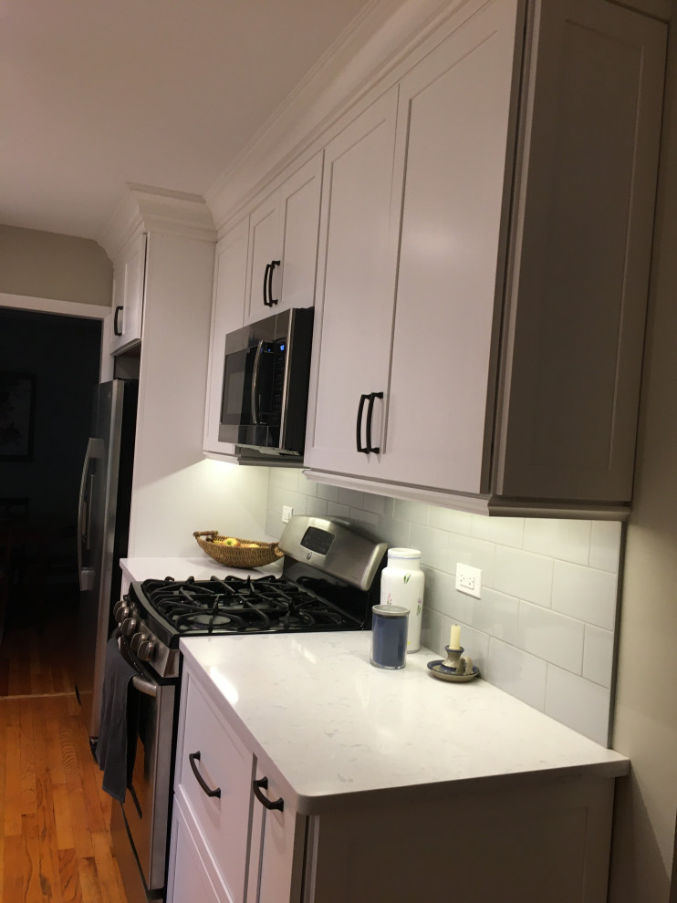 Photo of a small transitional l-shaped separate kitchen in Chicago with an undermount sink, shaker cabinets, white cabinets, quartz benchtops, grey splashback, ceramic splashback, stainless steel appliances, medium hardwood floors, no island, brown floor and white benchtop.