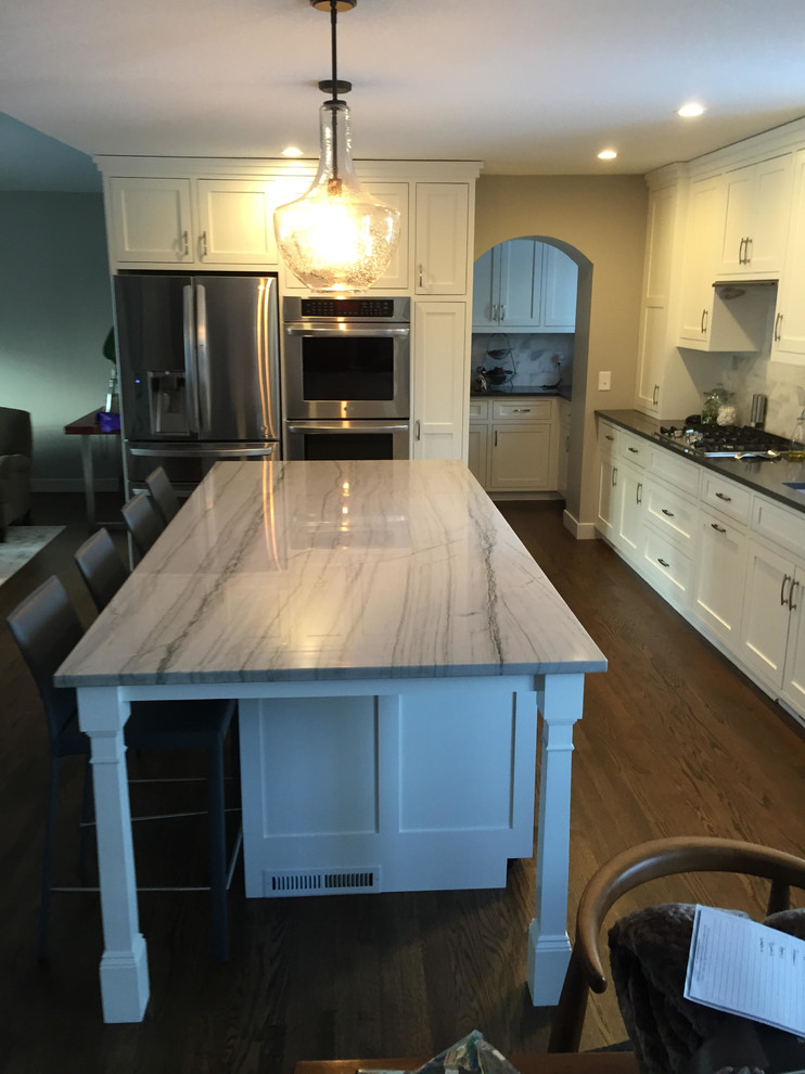 Large transitional dark wood floor and brown floor kitchen photo in Minneapolis with an undermount sink, shaker cabinets, white cabinets, quartzite countertops, gray backsplash, stone tile backsplash, stainless steel appliances and an island