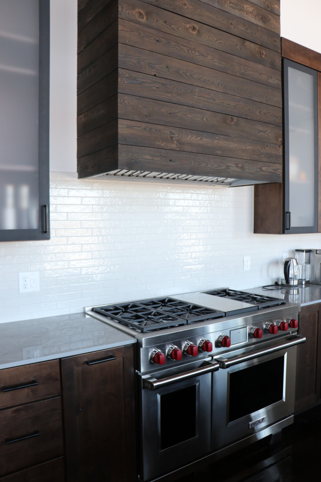Open concept kitchen - large rustic galley brown floor and vaulted ceiling open concept kitchen idea with an undermount sink, shaker cabinets, brown cabinets, quartz countertops, white backsplash, ceramic backsplash, stainless steel appliances, an island and white countertops