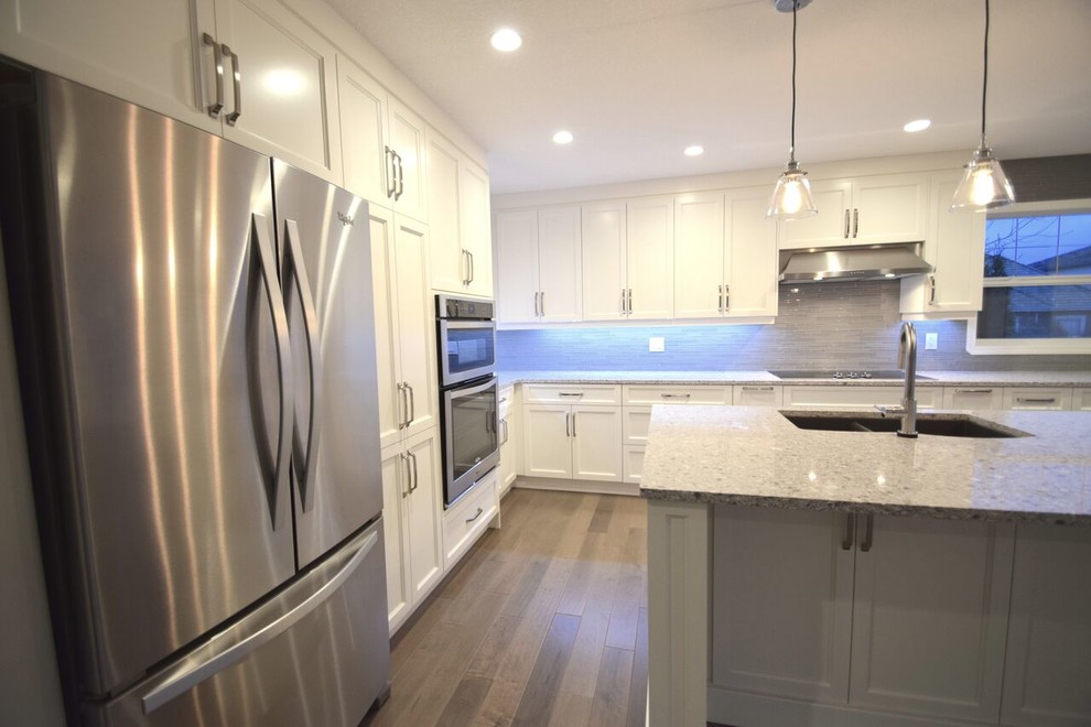 Transitional l-shaped vinyl floor eat-in kitchen photo in Edmonton with a double-bowl sink, shaker cabinets, white cabinets, quartz countertops, gray backsplash, glass tile backsplash, stainless steel appliances and an island