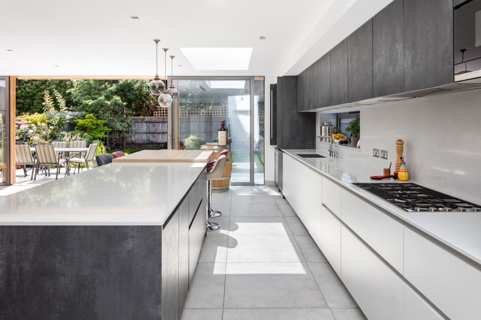 Inspiration for a mid-sized contemporary galley open plan kitchen in London with a drop-in sink, flat-panel cabinets, grey cabinets, granite benchtops, white splashback, mirror splashback, panelled appliances, ceramic floors, with island, grey floor, white benchtop and recessed.