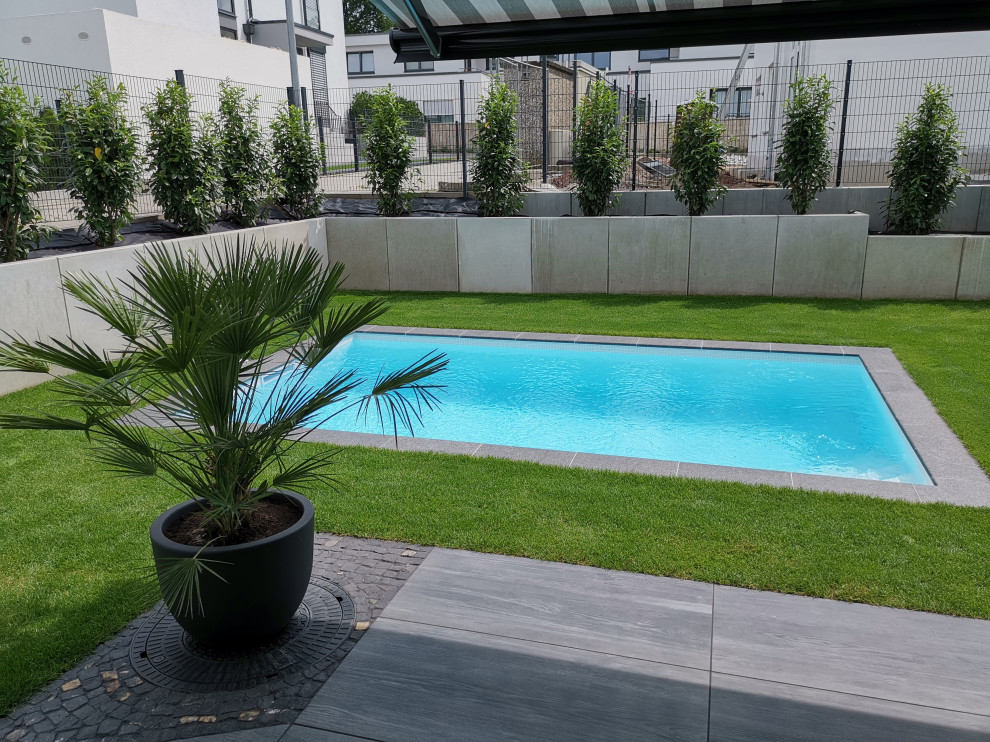 This is an example of a small contemporary side yard rectangular pool in Frankfurt with natural stone pavers.