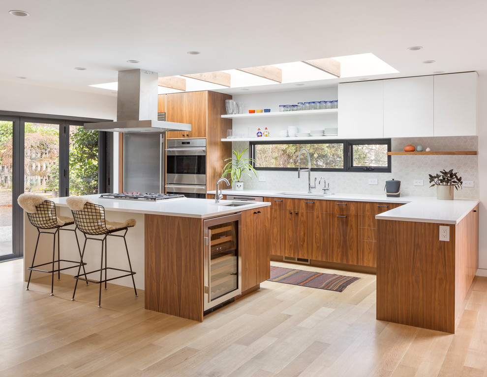 This is an example of a mid-sized midcentury l-shaped kitchen in Portland with an undermount sink, flat-panel cabinets, quartz benchtops, white splashback, ceramic splashback, stainless steel appliances, light hardwood floors, with island, white benchtop, white cabinets and beige floor.