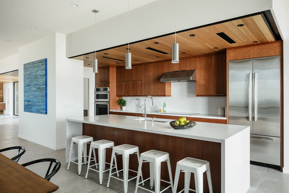 This is an example of a contemporary open plan kitchen in Phoenix with an undermount sink, flat-panel cabinets, medium wood cabinets, quartz benchtops, white splashback, stainless steel appliances, porcelain floors, with island, grey floor and white benchtop.