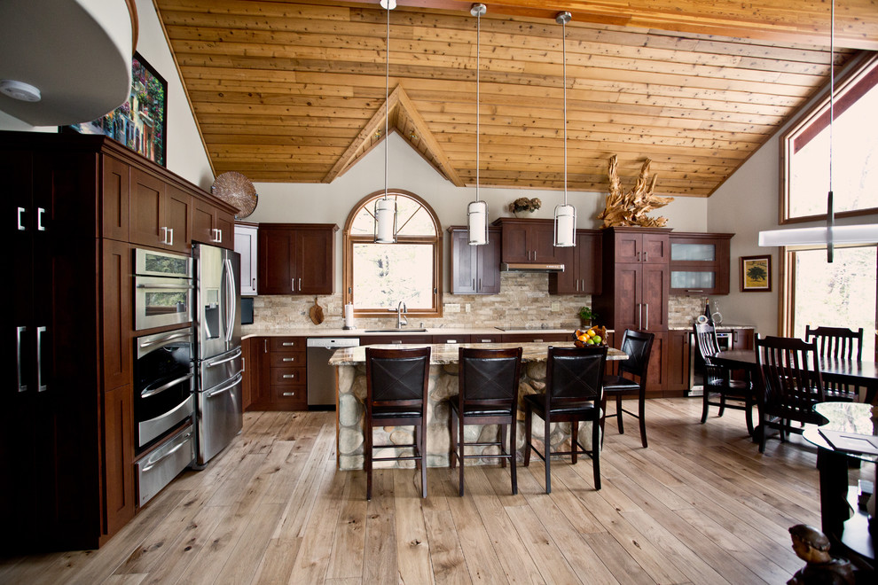 Eat-in kitchen - large rustic l-shaped light wood floor and beige floor eat-in kitchen idea in Toronto with an undermount sink, shaker cabinets, dark wood cabinets, granite countertops, beige backsplash, stone tile backsplash, stainless steel appliances and an island