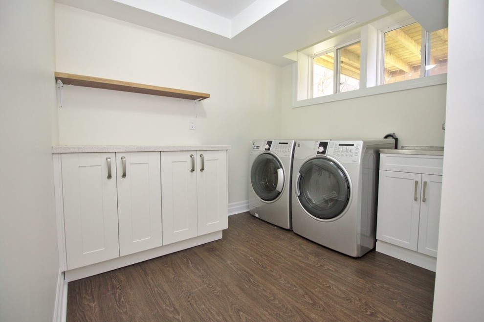 Dedicated laundry room - mid-sized transitional dark wood floor and brown floor dedicated laundry room idea in Toronto with shaker cabinets, white cabinets, stainless steel countertops, white walls and a side-by-side washer/dryer