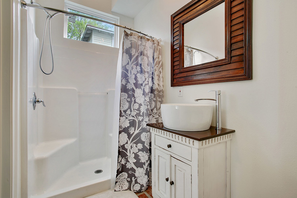 Photo of a large traditional 3/4 bathroom in New Orleans with a vessel sink, flat-panel cabinets, white cabinets, an alcove shower, white walls, brick floors, wood benchtops, red floor and a shower curtain.