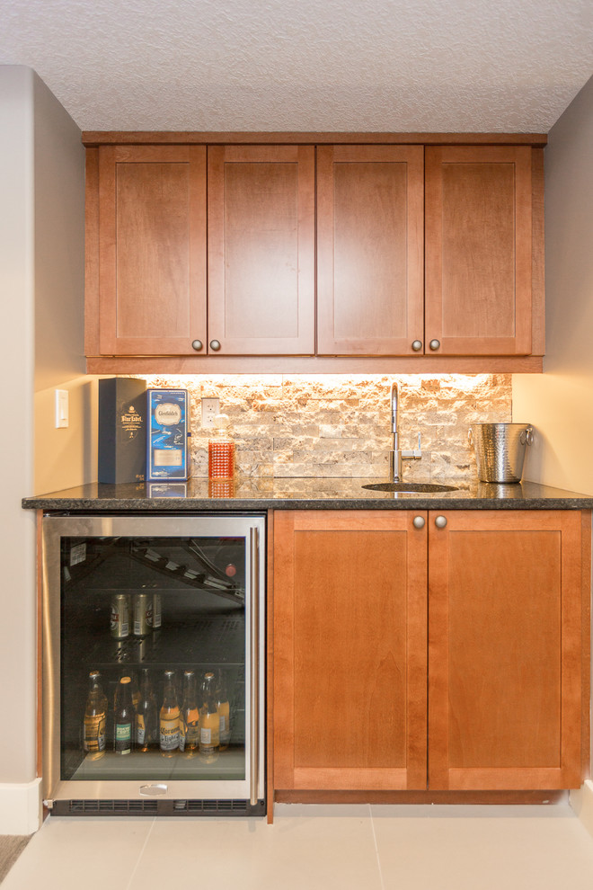 Design ideas for a small traditional single-wall wet bar in Calgary with an undermount sink, shaker cabinets, medium wood cabinets, granite benchtops, beige splashback, stone tile splashback and porcelain floors.