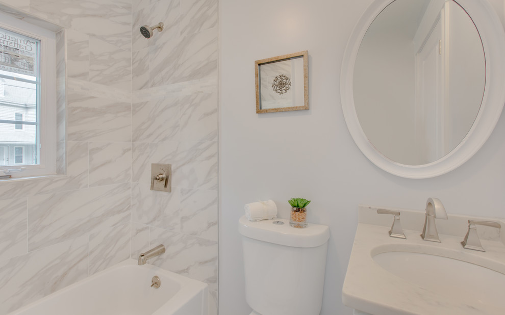 This is an example of a mid-sized transitional 3/4 bathroom in Boston with shaker cabinets, white cabinets, an alcove tub, a shower/bathtub combo, a two-piece toilet, gray tile, marble, grey walls, marble floors, an undermount sink, marble benchtops, grey floor, a shower curtain and white benchtops.