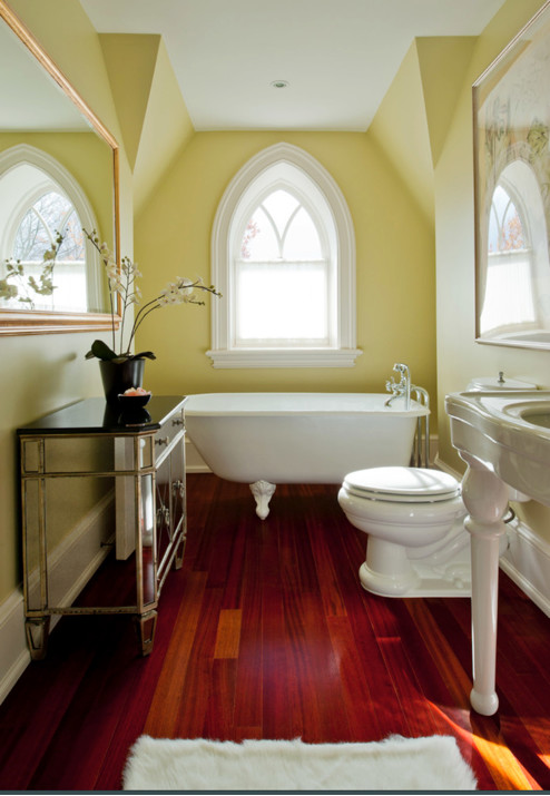 Immagine di una piccola stanza da bagno padronale country con vasca con piedi a zampa di leone, WC a due pezzi, pareti gialle, parquet scuro e lavabo a colonna