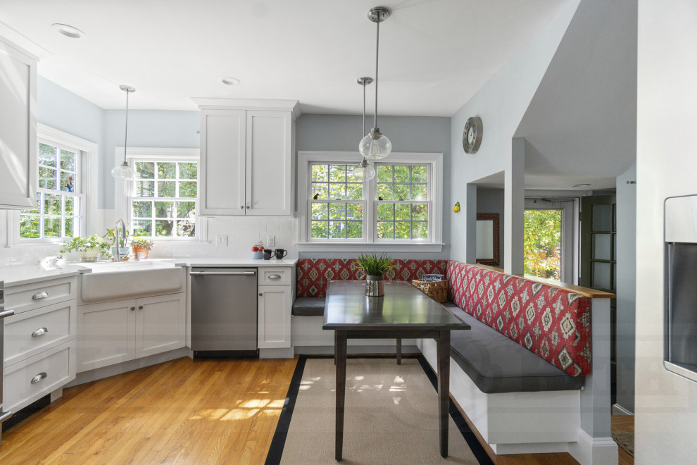 Example of a mid-sized transitional u-shaped medium tone wood floor enclosed kitchen design in Providence with a farmhouse sink, shaker cabinets, white cabinets, quartz countertops, white backsplash, ceramic backsplash, stainless steel appliances, no island and white countertops