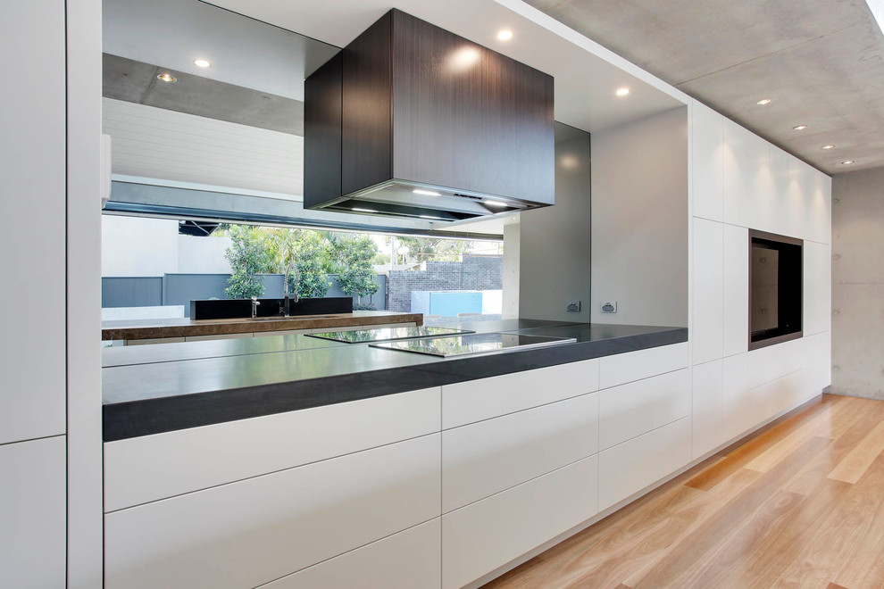 Inspiration for an expansive modern l-shaped eat-in kitchen in Sydney with an undermount sink, flat-panel cabinets, beige cabinets, marble benchtops, grey splashback, glass sheet splashback, black appliances, medium hardwood floors and with island.