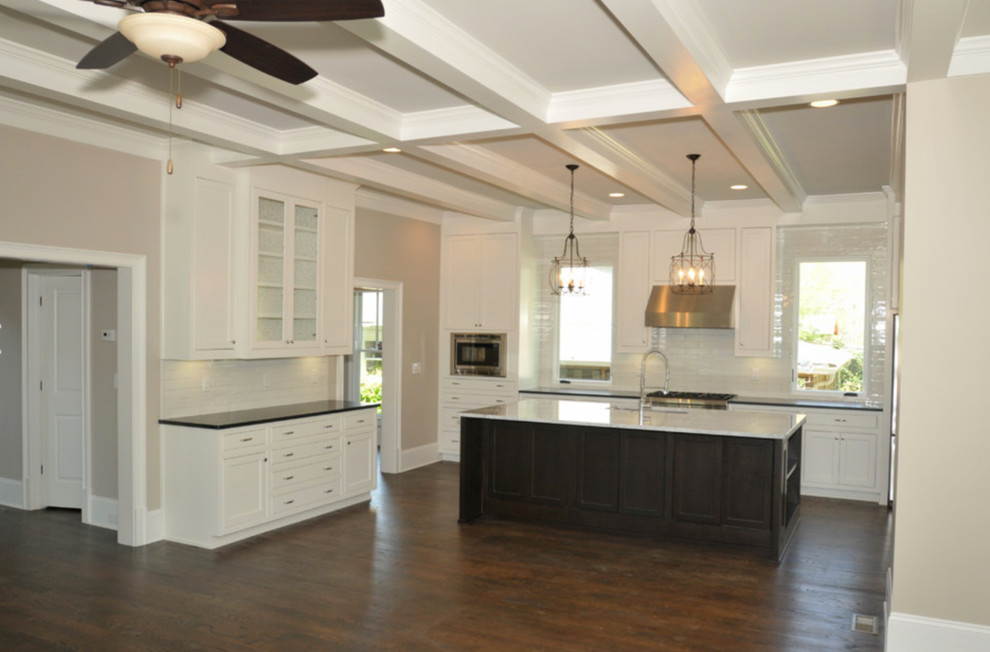 Open concept kitchen - large transitional l-shaped dark wood floor and brown floor open concept kitchen idea in Atlanta with a farmhouse sink, shaker cabinets, white cabinets, quartzite countertops, white backsplash, ceramic backsplash, stainless steel appliances and an island